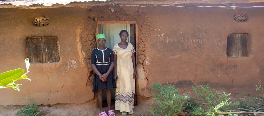 Aisha and her mother Mary Auma outside their old mud house