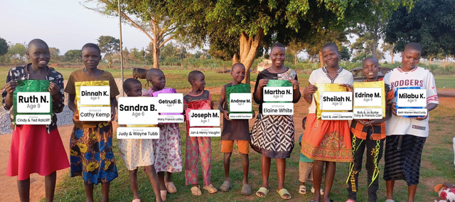 Ten children at Great Love Junior Academy holding cards with their name, age and sponsor, celebrating their August birthdays