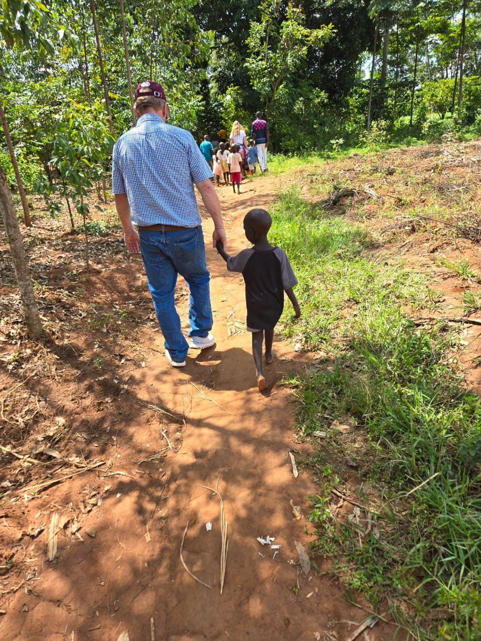 A small child holding Max&rsquo;s hand on the path out of the village