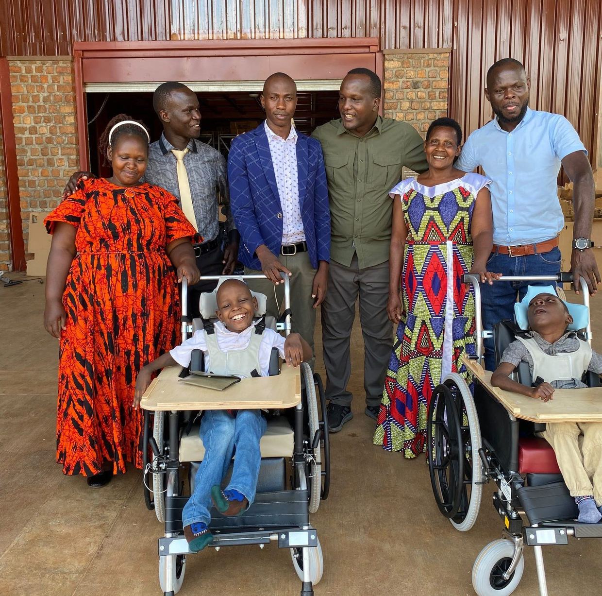Mark and Solomon in their new wheelchairs with their caregivers and the men who took them to Kampala