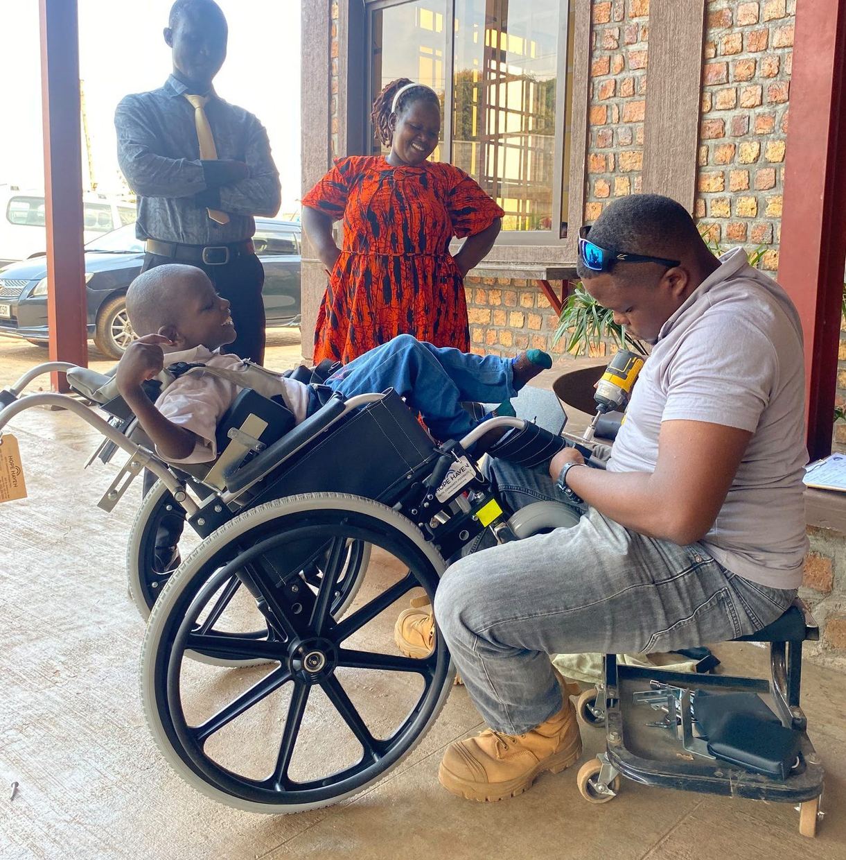 A technician adjusting Mark’s wheelchair while Mark sits in it and his caregiver looks on