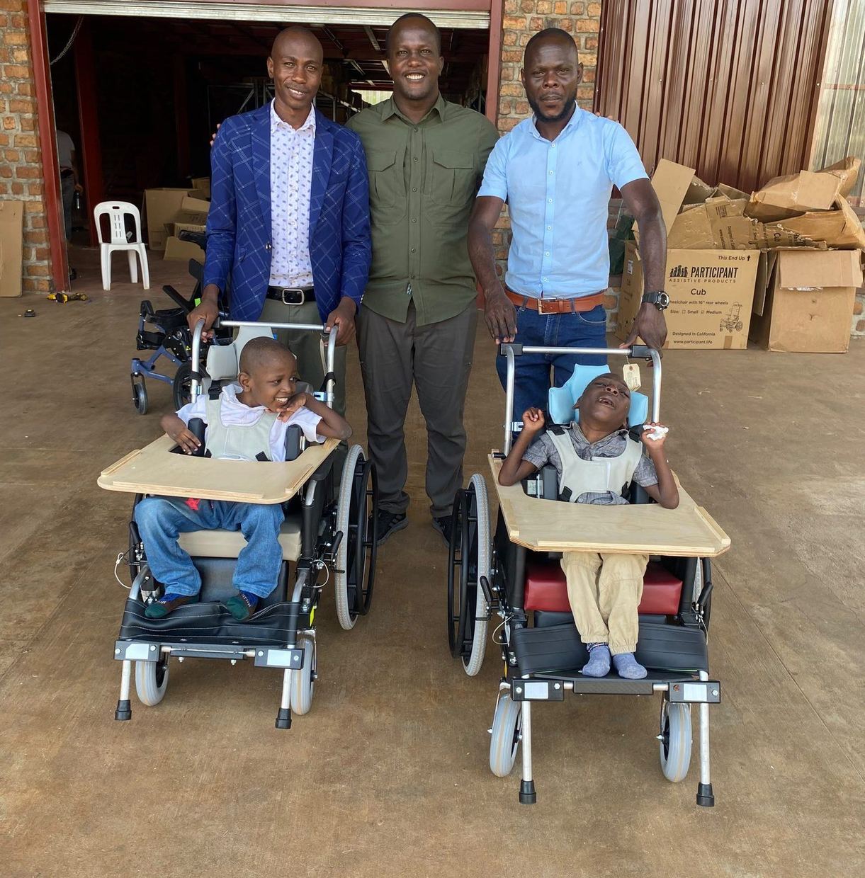 Pastor Isaac, Enock Nkulanga and George Musoke standing behind Mark and Solomon in their new wheelchairs