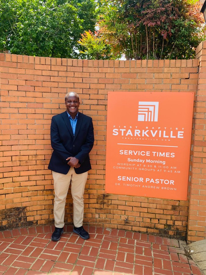 Enock Nkulanga standing beside the First Baptist Starkville sign