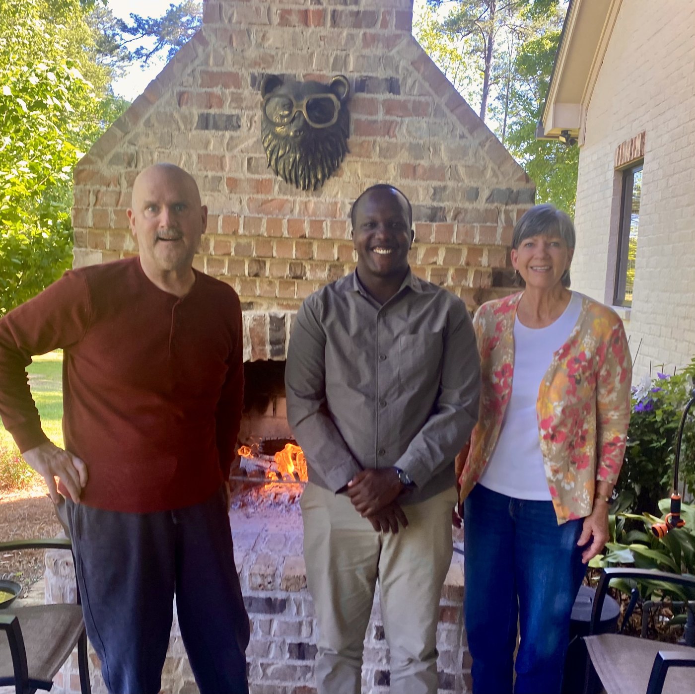 Enock with Cheryl and Tee Turner in front of an outdoor brick fireplace